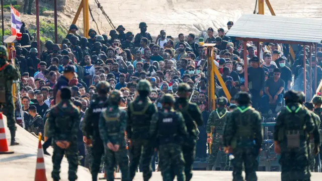 ወደ ታይላንድ ለመግባት ድንበር የቆሙ ብዙ ሰዎች እና ከፊት ለፊታቸው የቆሙ ወታደሮች