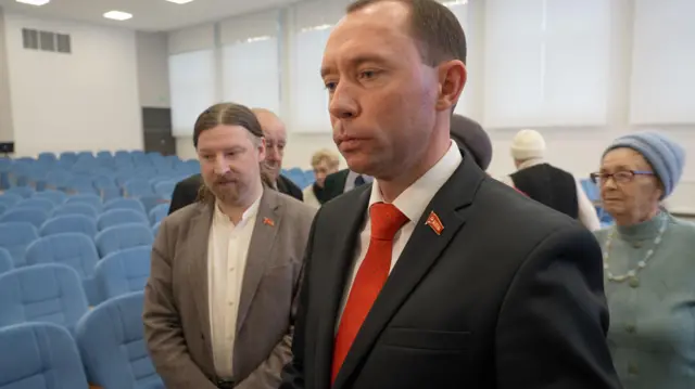 Sergei Syrankov wears a suit with a red tie and a Communist party pin.