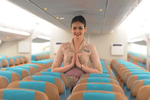 Seorang pramugari Garuda Indonesia sedang berdiri di tengah kursi-kursi kosong pesawat.