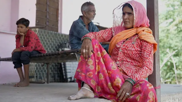 मुन्ना की मां अपने घर के आंगन में बैठी हैं. उनके पीछे उनके पति और बेटा पीछे बैठे हैं.