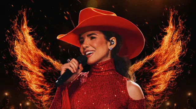 Paula Fernandes canta ao microfone usando um chapéu vermelho de abas largas e uma roupa vermelha brilhante com recortes nos ombros. Ao fundo, há grandes chamas formando uma espécie de asas sobre um palco escuro.