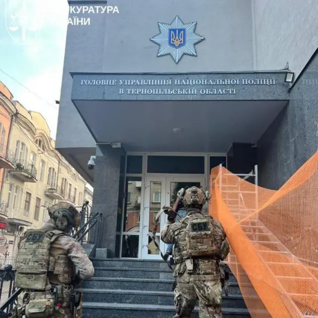 У входа в здание с надписью «Главное управление Национальной полиции в Тернопольской области» двое вооруженных силовиков в форме поднимаются по лестнице. На их спинах видны нашивки «СБУ», они держат оружие и направляются к двери.
