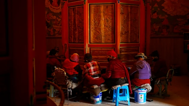 Mujeres tibetanas sentadas junto a una rueda de oración dentro de un monasterio.