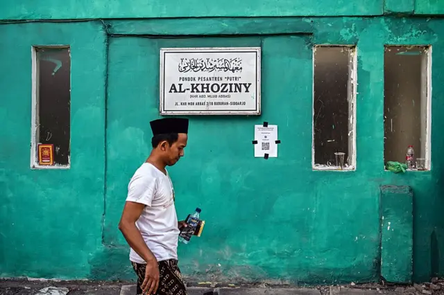 Seorang pria berjalan melewati papan nama Pondok Pesantren Al Khoziny saat operasi penyelamatan sedang berlangsung di lokasi bangunan runtuh di Sidoarjo, Provinsi Jawa Timur, pada 2 Oktober 2025,