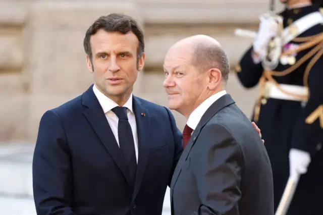 Emmanuel Macron ve Olaf Scholz el sıkışarak basına poz veriyor.