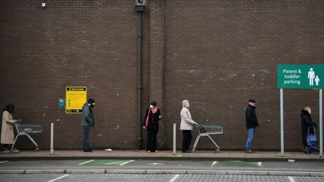একটি খাবারের দোকানের সামনে ক্রেতারা দূরে দূরে দাঁড়িয়েছেন।