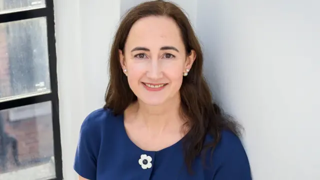 Sophie Kinsella (zdjęcie z 2018 r.), stojąca na tle białej ściany i okna.