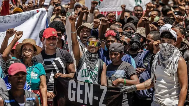 マダガスカルの首都で、多くの人が拳を振り上げて行進している。大半はキャップや帽子をかぶりっている。手前の人物は「GenZ（Z世代）」と書かれた布を掲げている