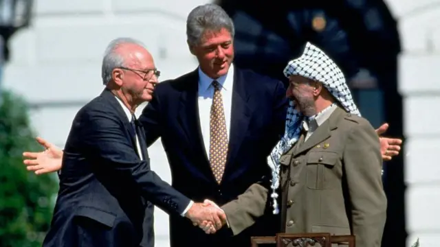 Isaac Rabin y Yasir Arafat se dan la mano frente a Bill Clinton.
