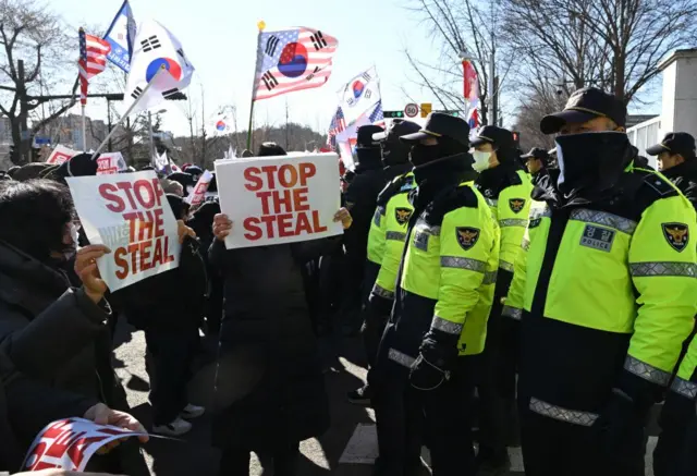 시위대가 부정선거 의혹을 제기하는 슬로건과 태극기, 성조기를 들고 경찰들 앞에서 시위하고 있다