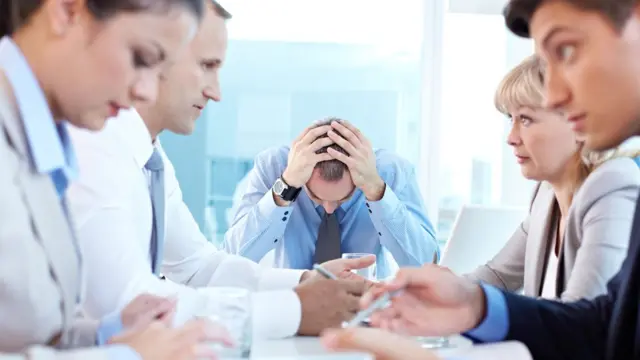 Una reunión con un hombre tomándose la cabeza.