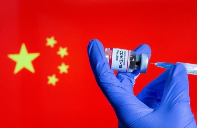 มือกำลังใช้เข็มฉีดยาดูดวัคซีนออกจากขวด ฉากหลังเป็นธงชาติจีน