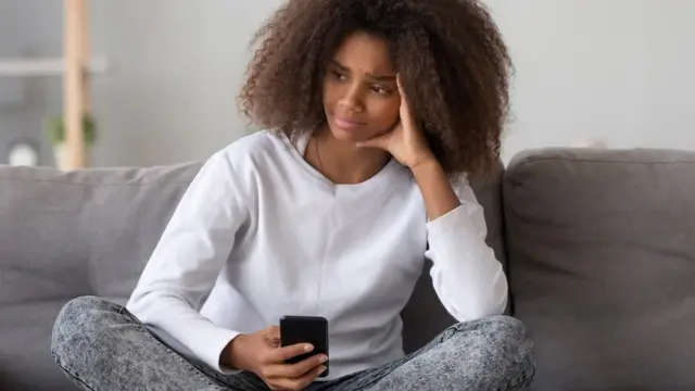 বিষন্ন এক নারী স্মার্টফোন হাতে ভিন্ন দিকে তাকিয়ে আছেন