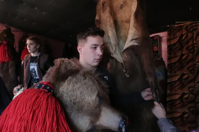 Mladići se pripremaju za početak ophoda po selu. Mečkarska grupa iz Asaua jedna je od najpoznatijih, a u ovom mestu se još uvek praktikuje stari običaj prema kojem povorka maskiranih meštana predvođena bubnjarima posećuje svaku kuću i izvodi ples.