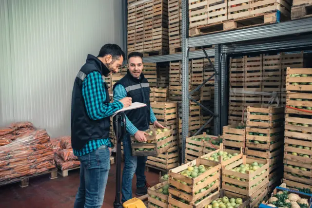 په سړې خونه کې دننه کارکوونکي د میوو کرېټونه ځای په ځای کوي.