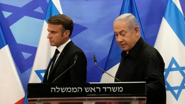 Presidente da França, Emmanuel Macron, ao lado do primeiro-ministro de Israel, Benjamin Netanyahu, em declaração pública, com bandeiras dos dois países ao fundo