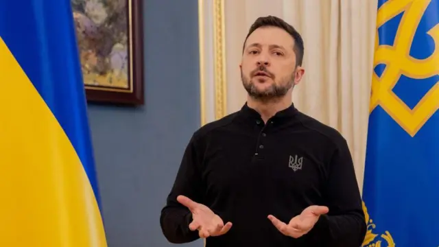 Le président de l'Ukraine tend les mains, entouré de deux drapeaux ukrainiens.