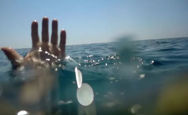 عکس کې ظاهرآ‌ سمندر ښکاري او د اوبو له منځه د لاس اورغوی او ګوتې راوتلې دی. ظاهرآ داسې ښکاري لکه څوک چې اوبو ډوب کړی وي. 