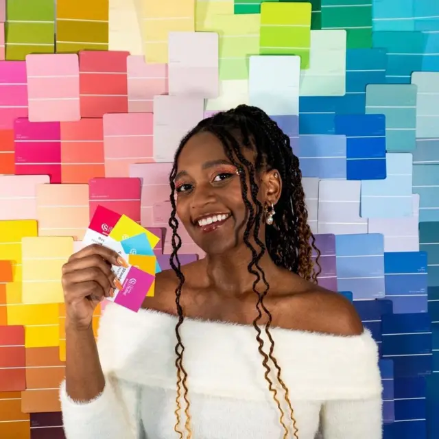 Micah Lumsden bir renk paletinin önünde duruyor ve elinde renk kartonları tutuyor. 