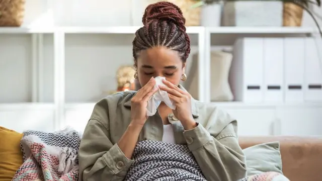 Woman sat under a blanket and blowing her nose