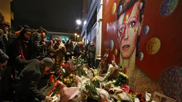 A woman leaves flowers beneath a Jimmy C mural of David Bowie in Brixton on January 11, 2016 in London