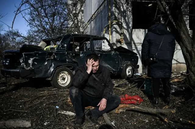 Người đàn ông ngồi bên ngoài một tòa nhà bị bom tàn phá ở Chuhuiv