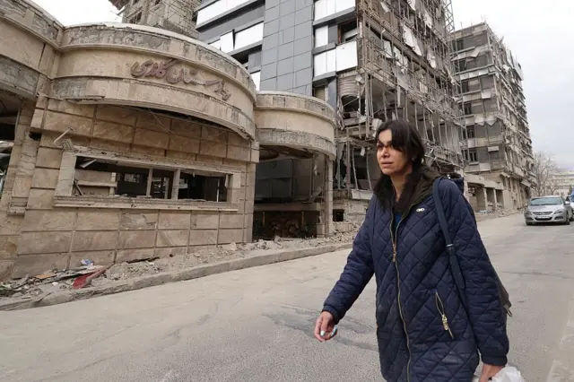 Mujer camina junto a edificios destruidos