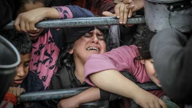 Umukobwa ugaragaza isura yuko ababaye ari hagati y’ibyuma, mu mbaga y’abantu barimo kubyiganira kugera ahatangirwa ibiribwa muri Rafah