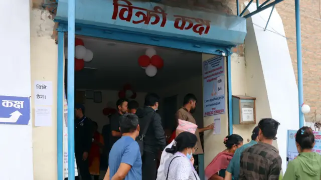 खाद्य कम्पनीको सुपथ मूल्य पसलमा टाँसिएको 'चिनी छैन' भन्ने सूचनाको छेउमा उभिएका उपभोक्ता 