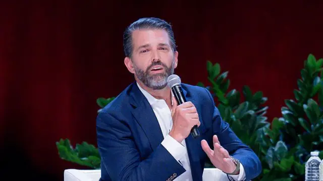 Donald Trump Jr, hijo de presidente, con un micrófono en mano, de chaqueta azul y camisa blanca, habla en una conferencia en Sugar Land, Texas. 23 de octubre 2025.