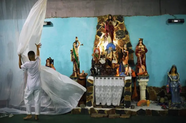 Homem abre cortina do congá (altar) com imagens de divindades 