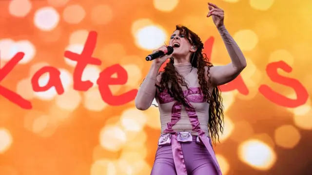 Kate Nash cantando no palco com uma roupa roxa,sites de apostas esportivas que aceitam pixum cenário laranja, com seu nomesites de apostas esportivas que aceitam pixletras gigantes