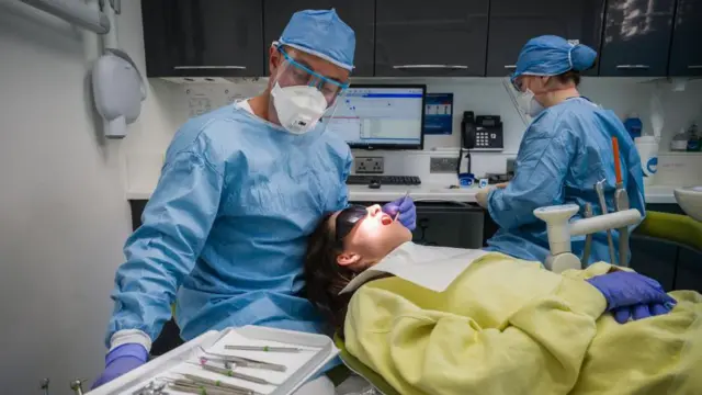 دندانپزشک فیض مغول (چپ) و پرستار دندانپزشکی جوآنا بارتا (راست)(R) روی یک بیمار در یکی از شش اتاق جراحی در مطب دندانپزشکی ایست ویلج در ۲۸ مه ۲۰۲۰ در لندن، انگلستان، دندان پر کردند