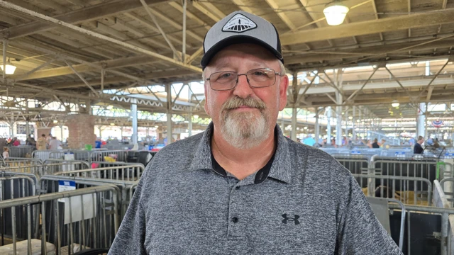 Un hombre con barba en primer plano lleva una gorra y se encuentra en una feria estatal.