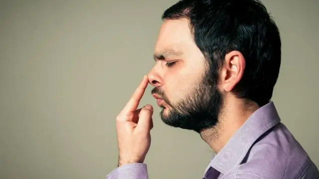 Un homme tenant son nez, les yeux fermés.