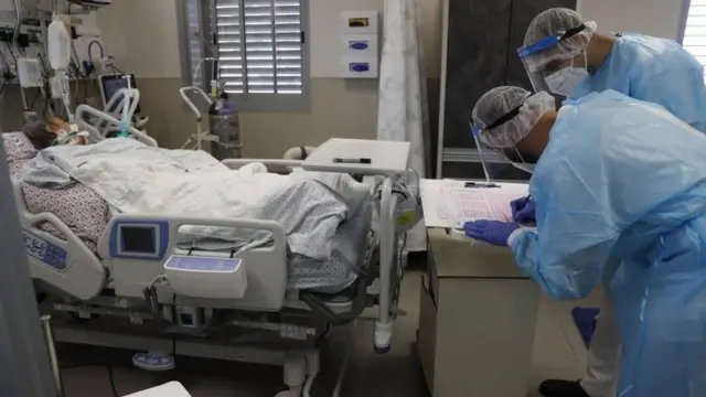 Paciente deitada e dois enfermeiros em sala de hospital