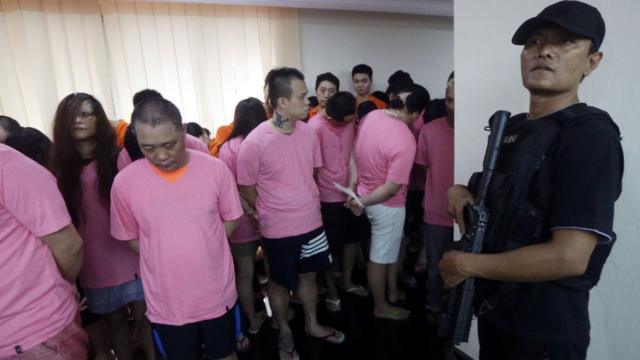This photo taken on July 31, 2017 shows an Indonesian policeman (in black) standing guard next to Chinese nationals who were arrested for alleged cyber fraud in Jakarta. Indonesia will deport 153 Chinese nationals arrested for alleged involvement in a multimillion-dollar cyber fraud ring targeting wealthy businessmen and politicians in China, police said on August 1