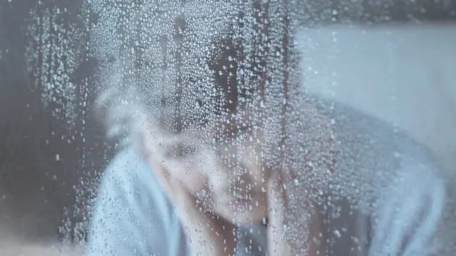 Una mujer mira a través de una ventana con lluvia