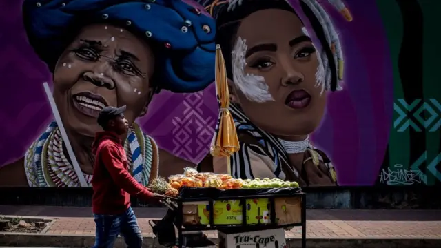 A rana guda wani mai sayar da kayan marmari na wucewa ta gaban wani zane da aka yi a kan titi a birnin Johannesburg...