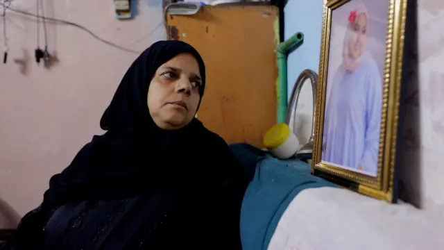 صورة لأم تنظر لصورة ابنتها المتوفاة