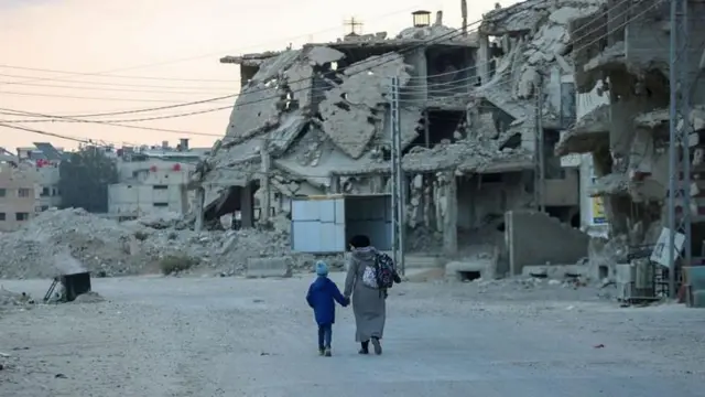 أم وطفلها يسيران وسط ركام مباني عدة