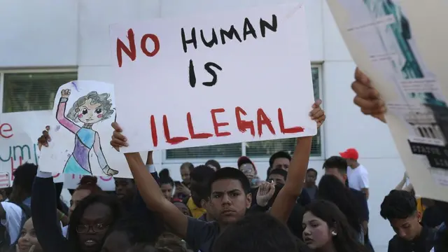 Un joven sostiene un cartel con la leyenda "No human is illegal": Ningún ser humano es ilegal.