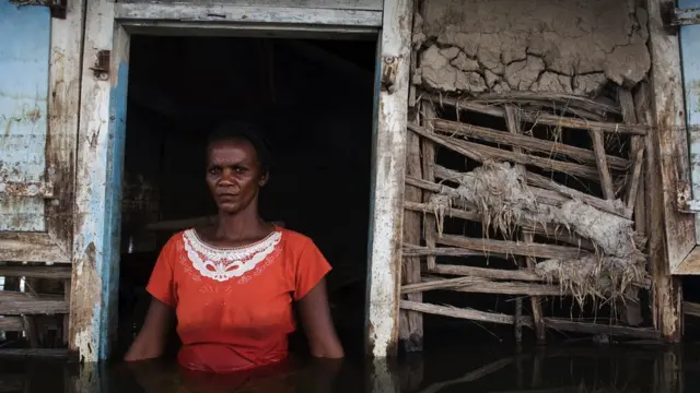 Adlene Pierre, aged 35, faces the camera in the doorway of her flooded house in the city of Gonaives, Haiti, after a hurricane in 2008