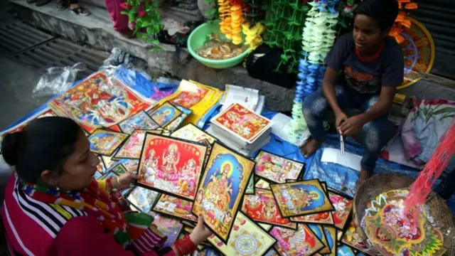 ஜம்முவில், தீபாவளியை முன்னிட்டு தெய்வங்களின் புகைப்படங்களை விற்பனை செய்யும் பெண்.