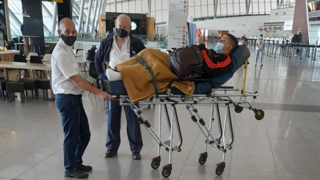 Douglas na maca no aeroporto, acompanhado de dois homens