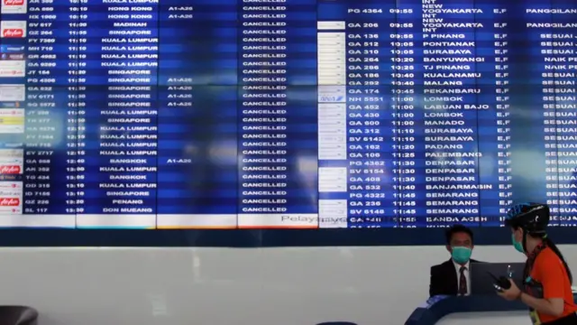 Petugas informasi bandara berada dibawah Monitor jadwal penerbangan yang memperlihatkan pengumuman dibatalkannya penerbangan di Terminal 3 Bandara Soekarno Hatta, Tangerang, Banten, Rabu (01/04).