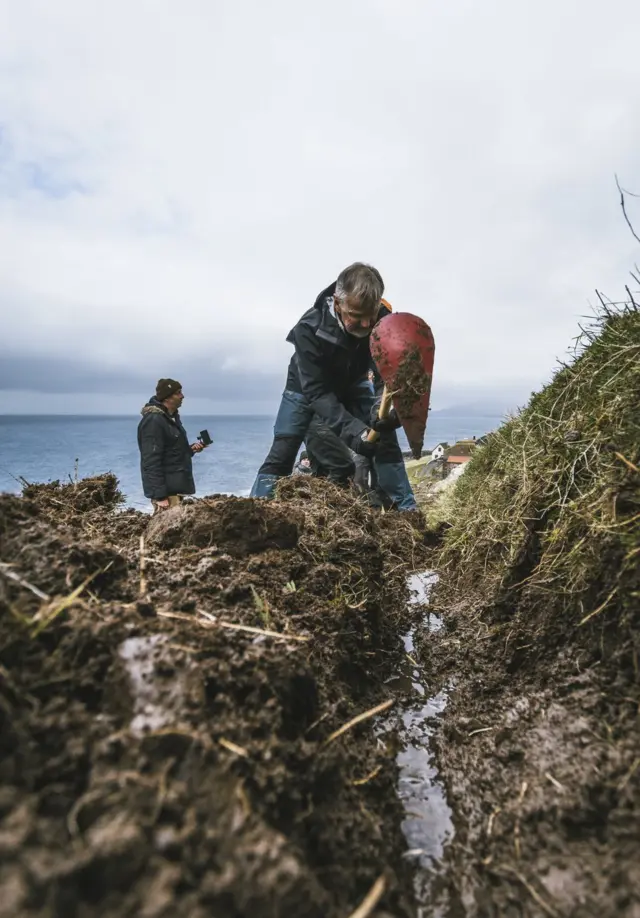 A green group voluntourist digs a water channel in Skarvanes
