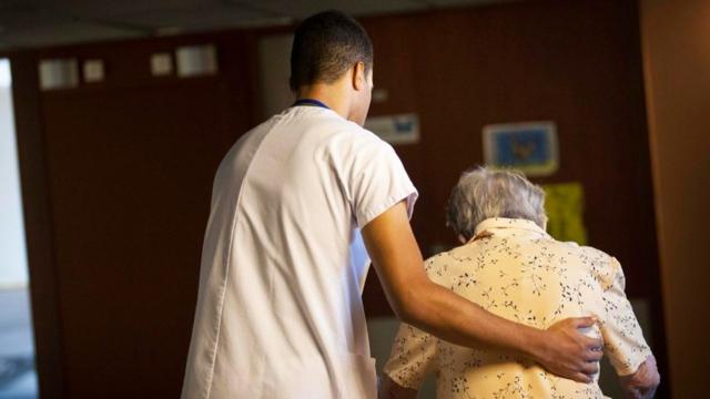 Un enfermero ayudando a caminar a una anciana