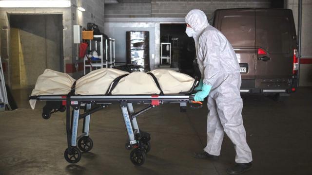 В испанской Жироне сотрудники похоронной службы в защитных костюмах перевозят тело жертвы коронавируса