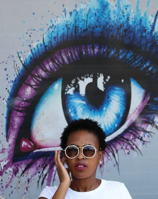 Umusi umwe imbere y'aho mu gisagara ca Randfontein kiri hafi ya Johannesburg, umugore yari yafashwe isanamu ahagaze imbere y'igisanamu kinini c'ijisho, ikimenyetso cerekana ko inzu ari ivuriro ry'amaso